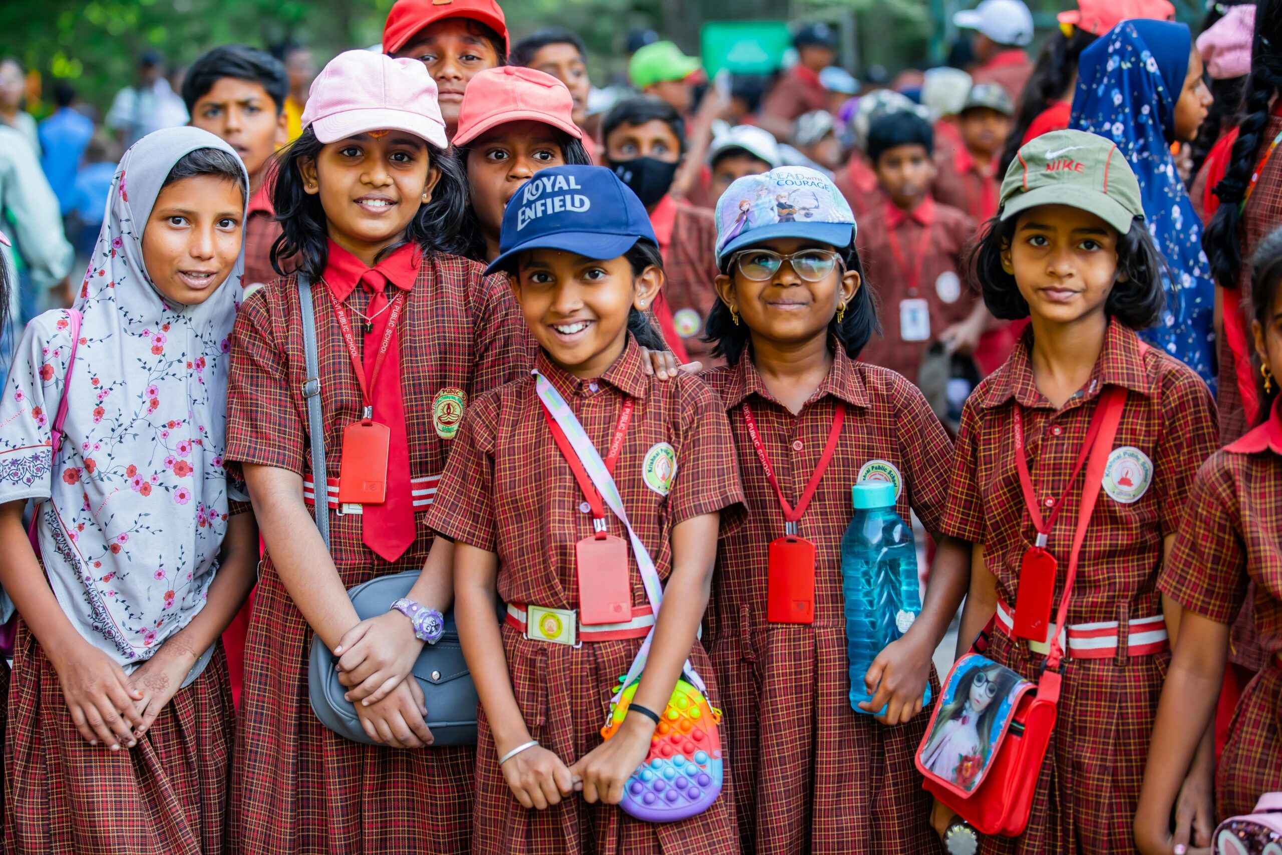 A cheerful group of school children smiling outdoors in uniforms with ID cards.